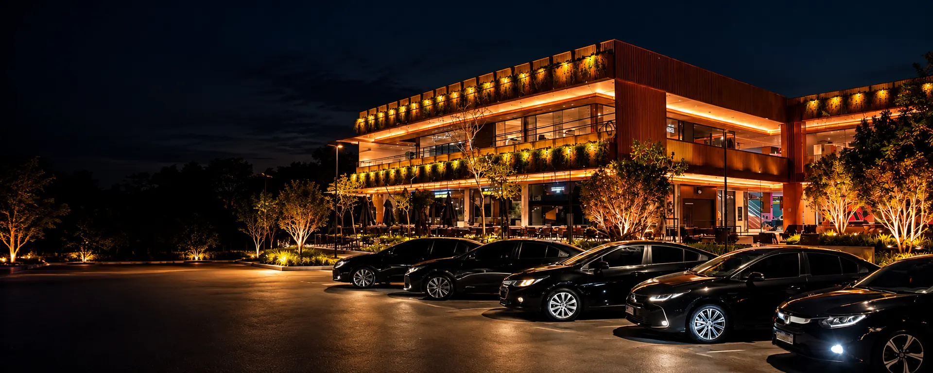 Frota de sedans executivos pretos da C.A. Transporte Executivo à noite, em frente a restaurante iluminado